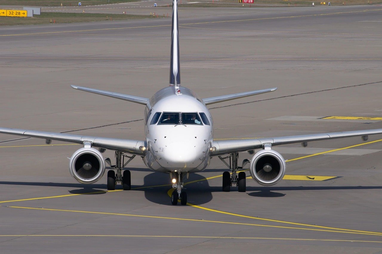 Parked commercial aircraft at airport terminal with ground service vehicles nearby.