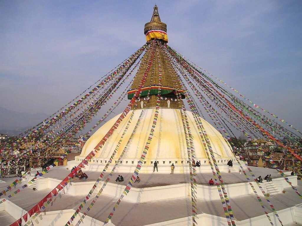 Aerial view of the Boudhanath Stupa with colorful prayer flags fluttering around the giant white dome and golden spire in Kathmandu, Nepal.