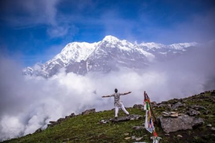 A man posing for pictures with the majestic Annapurna mountain ranges in the background under a clear blue sky.