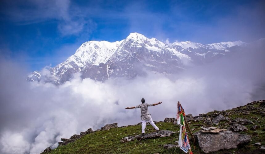 A man posing for pictures with the majestic Annapurna mountain ranges in the background under a clear blue sky.