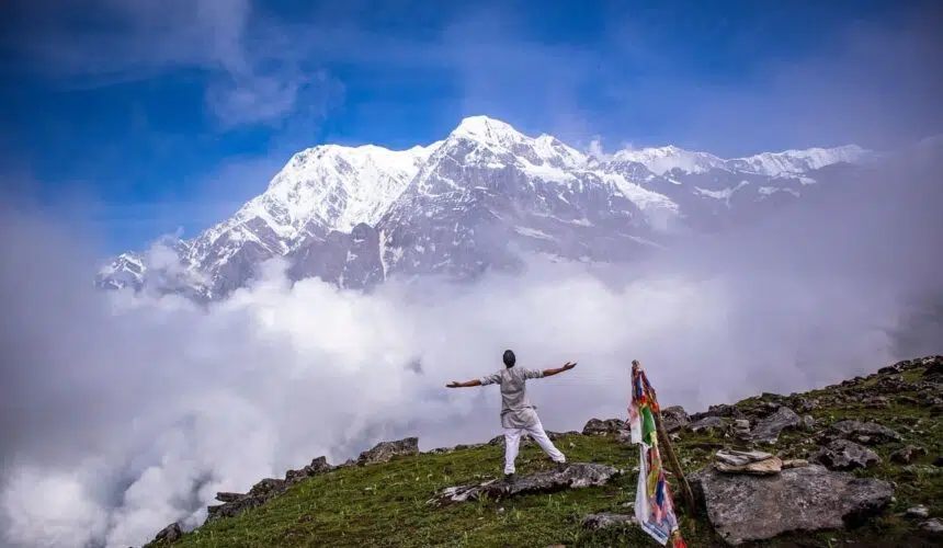 A man posing for pictures with the majestic Annapurna mountain ranges in the background under a clear blue sky.