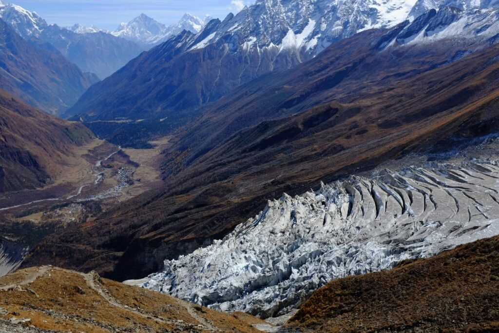 A breathtaking view of Samagaun village as seen from Manaslu Base Camp, nestled in a wide valley with traditional stone houses, alpine meadows, and majestic Himalayan mountains in the distance.