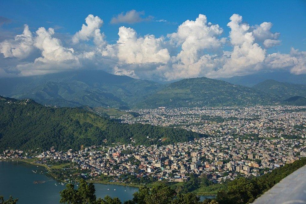 Scenic view of Pokhara city with buildings, green hills, and mountains in the background, Nepal.